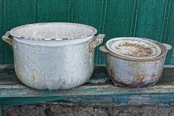 old dishes from dirty bowls and pans stand on a gray table against a green wall