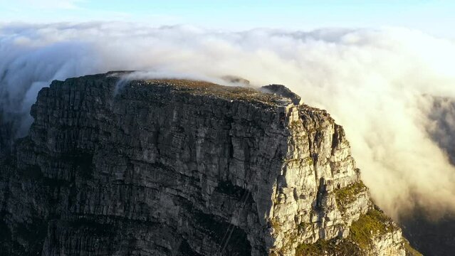 Backward tracking aerial shot looking down at a massive bank of clouds blowing over the top of Table Mountain Cape town.
