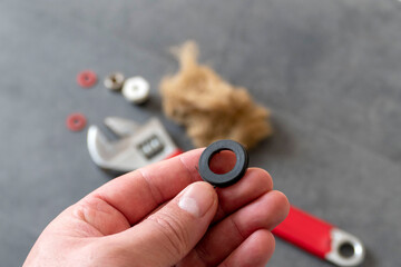 A plumber has a water seal in his hand- On the floor, there is a wrench and a plumbing linen.