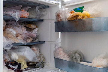 Frozen foods are in a freezer with the door open, a messy inside of a deep freezer, - obrazy, fototapety, plakaty