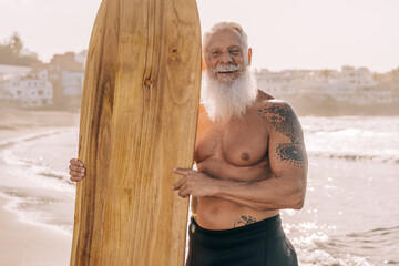 Happy senior surfer man holding vintage wood surf board on the beach - Focus on face