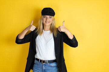 Beautiful woman wearing casual white t-shirt and a cap over isolated yellow background success sign doing positive gesture with hand, thumbs up smiling and happy. cheerful expression