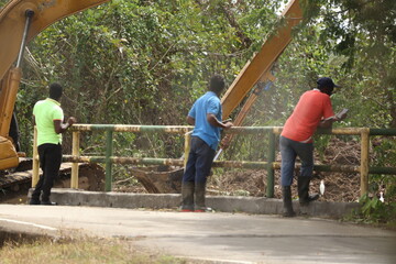 three workers on a Caribbean bridge in Trinidad looking at a digger doing work