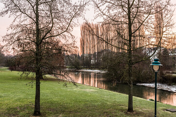 Idyllic view over a pond, bare trees and meadows covered with a thin snowlayer in the Baudouin park during sunrise, Jette, Belgium