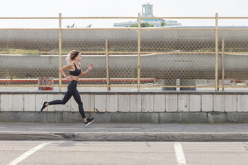 athletic fit woman running outdoor on urban street, side view