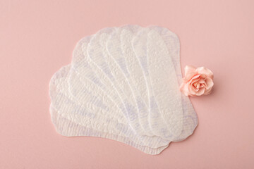 White sanitary pads, hygiene protection on a pink background. Gynecological menstrual cycle. A rose flower lies on a menstrual pad. First menstruation