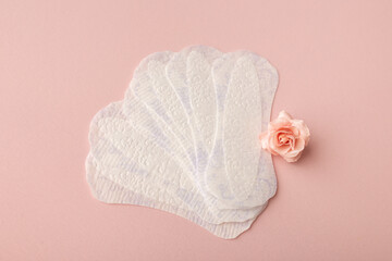White sanitary pads, hygiene protection on a pink background. Gynecological menstrual cycle. A rose flower lies on a menstrual pad. First menstruation