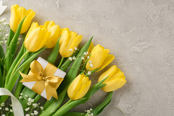 Top view photo of woman's day composition white giftbox with golden bow bouquet of yellow tulips white gypsophila and white ribbon on isolated textured grey concrete background with copyspace
