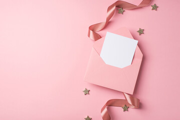 Top view photo of valentine's day decorations curly silk ribbon open pink envelope with paper sheet and small glowing stars on isolated pastel pink background with blank space