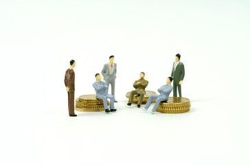 On the white surface on the coins and next to them are miniature figures of businessmen conferring.