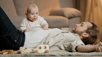 Caucasian family father with little daughter son lie on floor at home play. Baby girl boy newborn kid crawling over daddy child care fatherhood nursery indoors. Children parenthood childhood love