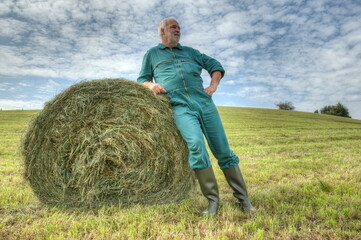 Naklejka na ściany i meble Farmer makes after hay harvest a break and enjoy the moment between the round hay bales on the mown meadow.