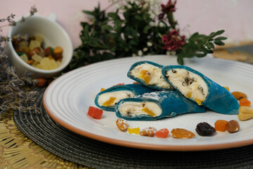Colored fried pancakes. on a white plate. Turquoise and blue bliny. Stuffed with sweet cottage cheese with dried apricots, prunes, nuts. Delicious stuffing. Maslenitsa, food festival. Children's menu.