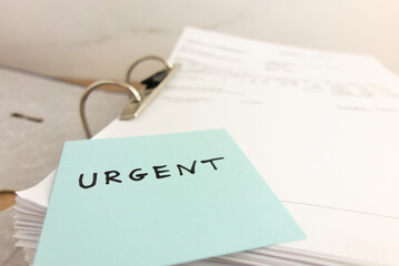 Sticky note with word urgent lying on stack of business paper files