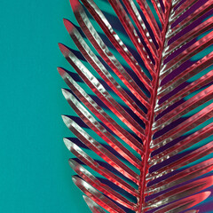 Trendy retro composition of a golden palm tree leaf on a vivid turquoise background with red neon accents.