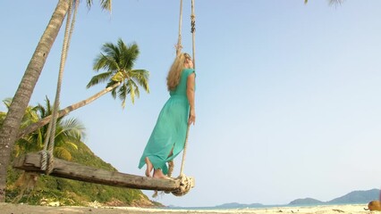 Woman spends her vacation at the seaside. The girl is swinging on a swing. Concept meditation, relaxation and walks, replenishment of energy and good happy mood.