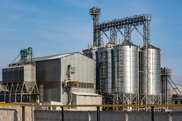 agro silos granary elevator in winter day in snowy field. Silos on agro-processing manufacturing plant for processing drying cleaning and storage of agricultural products, flour, cereals and grain.