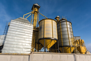 agro silos granary elevator in winter day in snowy field. Silos on agro-processing manufacturing plant for processing drying cleaning and storage of agricultural products, flour, cereals and grain.