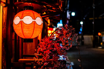 Kyoto, Japan colorful street road alley in Gion district at night evening with closeup of illuminated traditional red paper lantern lamp and cherry blossom sakura flowers decorations - Powered by Adobe