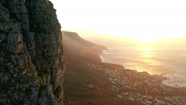 Aerial shot rising upward along the edge of Table Mountain Cape Town, during a dramatic sunset with the Twelve Apostles in the background.