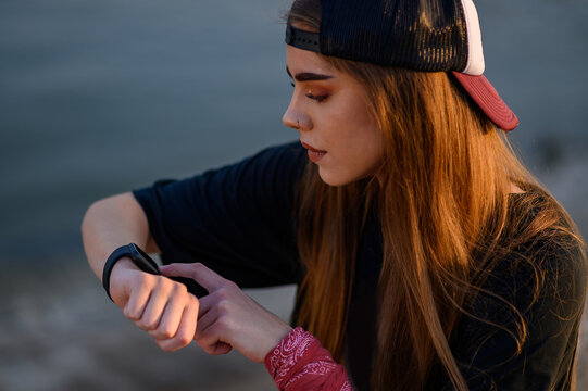 Young woman sitting near the river and checking her smartwatch