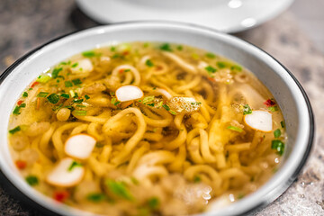 Macro closeup of Japanese udon ramen noodle instant soup in bowl as asian meal with texture of toppings floating such as fish cakes and green onion