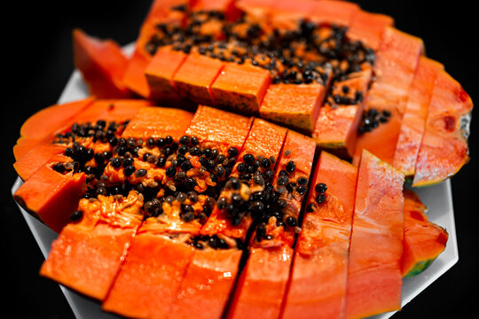 Closeup macro of large Caribbean red ripe papaya fruit sliced two halves slices with fresh orange red colorful flesh cut in half on plate with black background and seeds