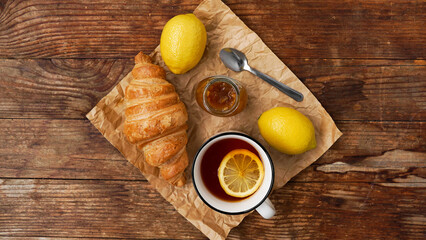 Fototapeta na wymiar Lemon tea, home made jam, croissant on wooden table. Breakfast concept. Top view