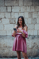 Beautiful young woman using smartphone while walking on the city streets on the coast