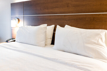 Bedroom empty room with illuminated lit lamp light and closeup of four white pillows with sheets on mattress bed headboard in modern hotel with nobody