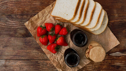 Slices of bread and delicious strawberry jam jar and fresh berries on wooden table. Ingredients for making toast for a delicious breakfast.