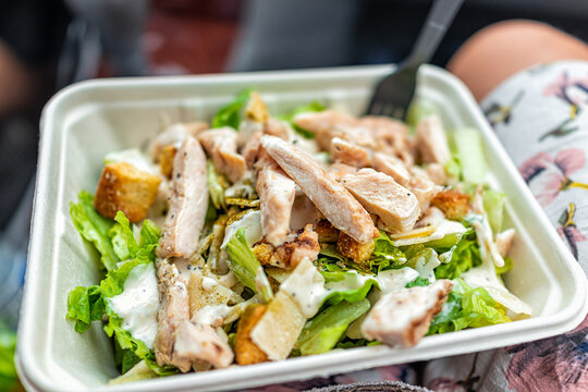 Closeup of fresh creamy caesar dressing salad with chopped vegetables romaine lettuce greens and grilled chickens strips in tray carton as quick fast lunch in car on road trip