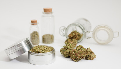 top view of marijuana buds with grinder accessories, glass bottles, and white background