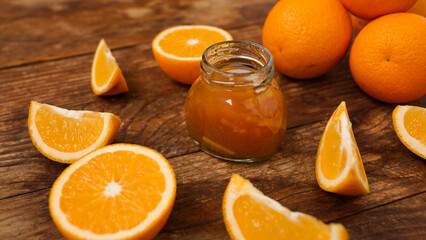 Jar of orange jam on wooden background from top view. Homemade orange marmalade, confiture in thick syrup.