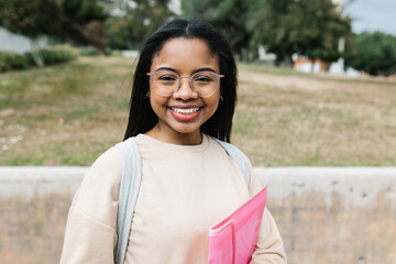 Portrait of smiling young hispanic latina student girl holding file while standing at campus school...