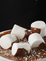 Appetizing white marshmallow pieces in chocolate paste isolated on black background. Sweet food, pastry shop, breakfast, holiday, birthday, supermarket, banner.