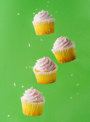 original composition. Cupcakes with pink cream in frozen flight on a light green background. birthday invitation, holiday. Cooking, baking, desserts, shop, pastry shop, banner.