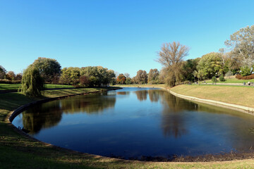Fototapeta na wymiar Pond and trees in the park on a warm autumn day. Kepa Potocka, Warsaw, Poland
