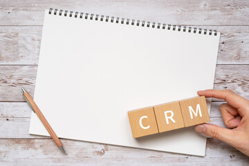 CRMのイメージ｜「CRM」と書かれた積み木、ペン、ノート、人の手