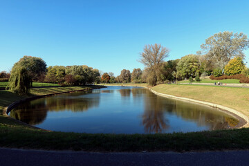 Fototapeta na wymiar Pond and trees in the park on a warm autumn day. Kepa Potocka, Warsaw, Poland