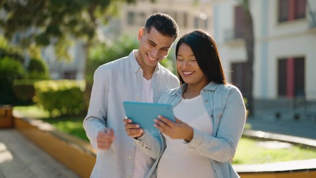 Young latin couple hugging each other using touchpad at park