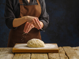 Dough on a wooden cutting board, prepared by the hands of a professional chef. Dark background. Preparation of dough products - bread, pizza, pasta, pie, confectionery. Cookbook.