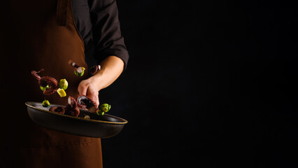 A professional chef prepares seafood - octopus with pieces of vegetables on a black background. Seafood cooking. Restaurant, hotel, cookbook. There is an empty space to insert.