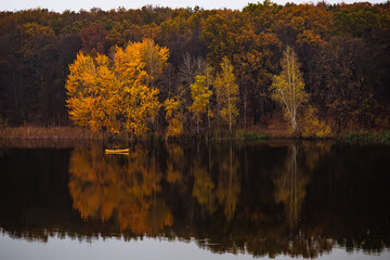 Yellow small boat near the forest with golden autumn trees