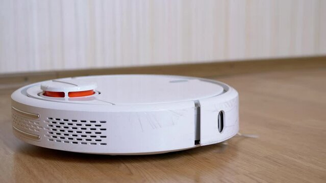A Modern Automatic Robot Vacuum Cleaner Sweeps Debris on Floor in Room. A rotation white vacuum cleaner with small brushes, touch motion sensor. Autonomous room cleaning. Smart home assistant. 4K.