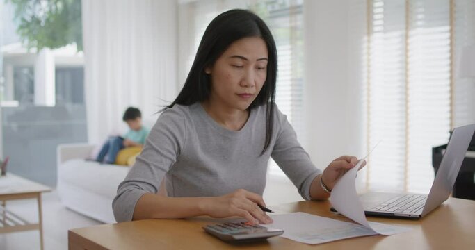 Adult asia people single mom small SME owner support happy sit busy apply child tax credit refund plan form app or pay loan bill on laptop. Little kid boy play at home hybrid job career workforce.