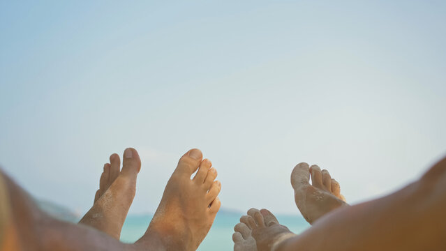 Bare feet of young man and woman couple wiggle lying on beach near calm azure ocean at exotic resort close first point view. Pov of leg of a couple of men and women lying on a tropical sandy beach.