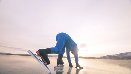 The child train on ice speed skating. The athlete at the start, in a sports stance. The kid girl skates in the winter in sportswear, sport glasses. Children speed skating short long track. Outdoor.
