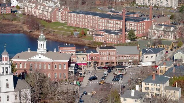 telephoto orbit drone view of downtown exeter, nh during christmas time. The focus is on the gazebo and town hall in the center of town with the exeter river and mill buildings in the background