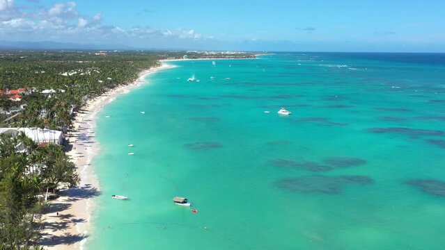Tropical coastline with resorts, palm trees and caribbean sea with floating boats and people having fun doing paraseiling. Travel destinations. Dominican Republic. Aerial view